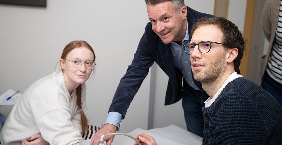 Ein Mädchen lässt ihre Finger von zwei Männern schallen, alle schauen auf einen Bildschirm mit den Ultraschallbildern.