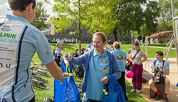 Ein Mann gibt einem Radfahrer eine blaue Tasche des Bundesverbandes.