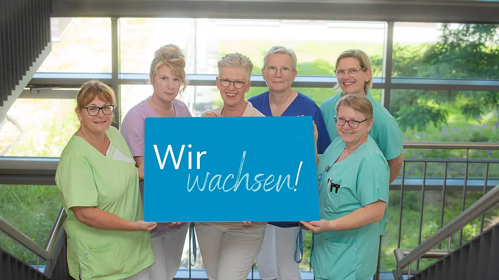 Pflegekräfte halten ein Schild in der Mitte auf dem steht "Wir wachsen".