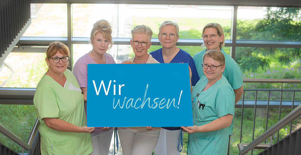 Pflegekräfte halten ein Schild in der Mitte auf dem steht "Wir wachsen".